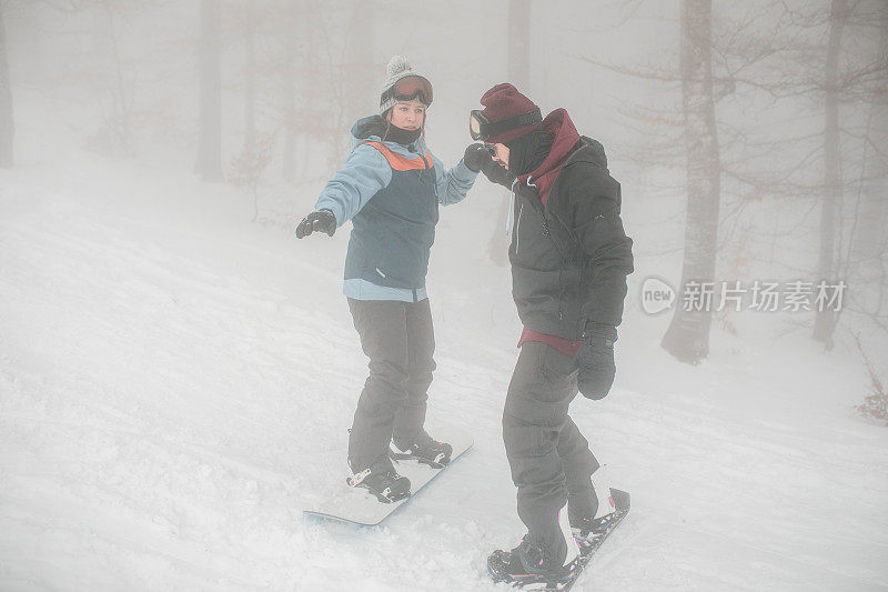 在一个雾蒙蒙的冬日，两名单板滑雪者正从斜坡上滑下，享受着冒险的乐趣