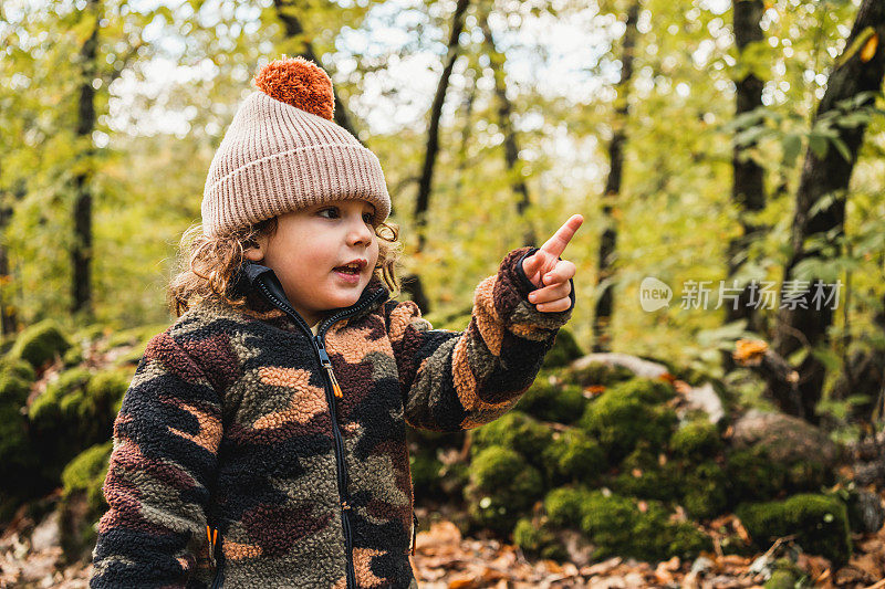 一个漂亮时髦的小男孩戴着帽子在森林里指着前方