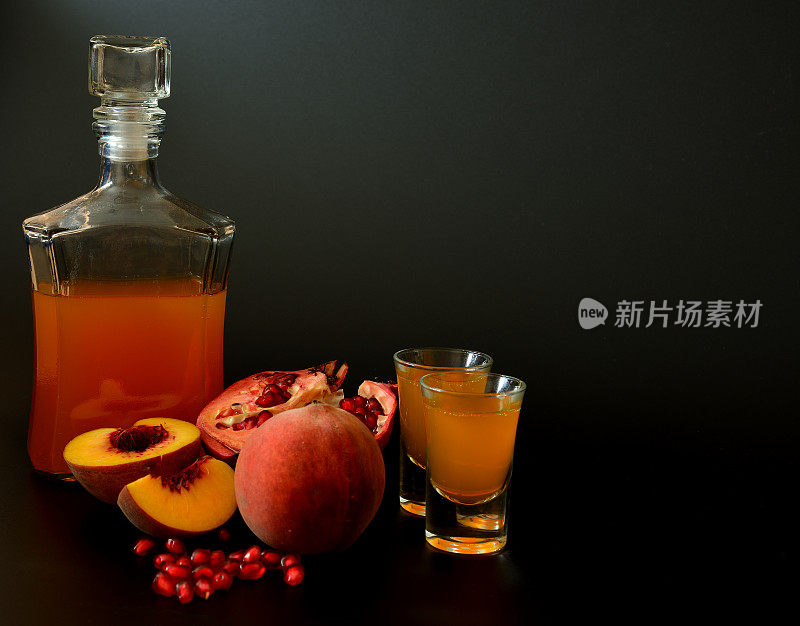 石榴桃利口酒，一种自制的烈性酒，装在一个玻璃瓶和两个玻璃杯里，背景是黑色的，旁边是成熟的水果。