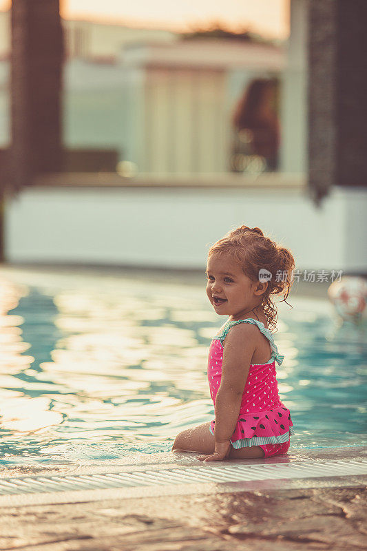 可爱的小女孩坐在游泳池边上