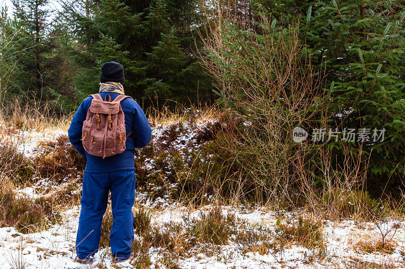 一个冬天的早晨，地上有一层小雪，一位老人背着帆布背包在一片森林里