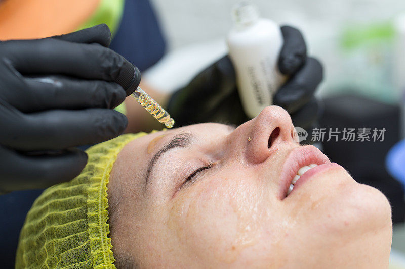 美容师用吸管将化妆品滴到女性脸上的皮肤上。