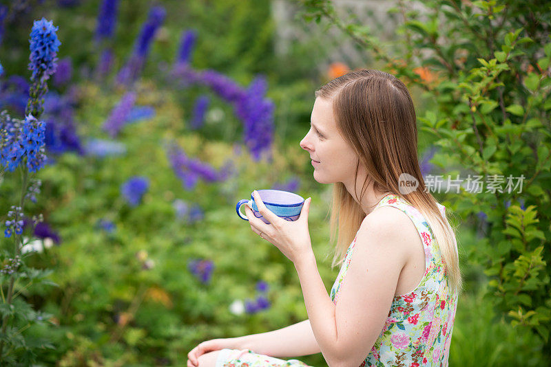 年轻女子拿着茶杯侧视侧面，坐在夏日花园。