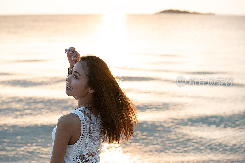 一个年轻女子的后视图，在日落时望向大海