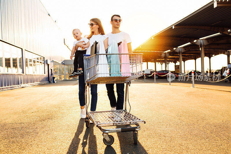 幸福的一家人带着孩子用购物袋和购物手推车在购物中心的后台，一家人一起购物