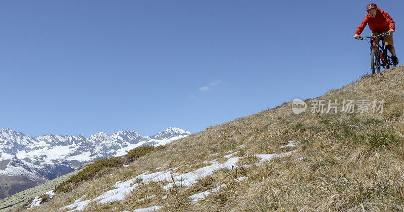 骑山地车的人在白雪覆盖的山峰上骑下田野