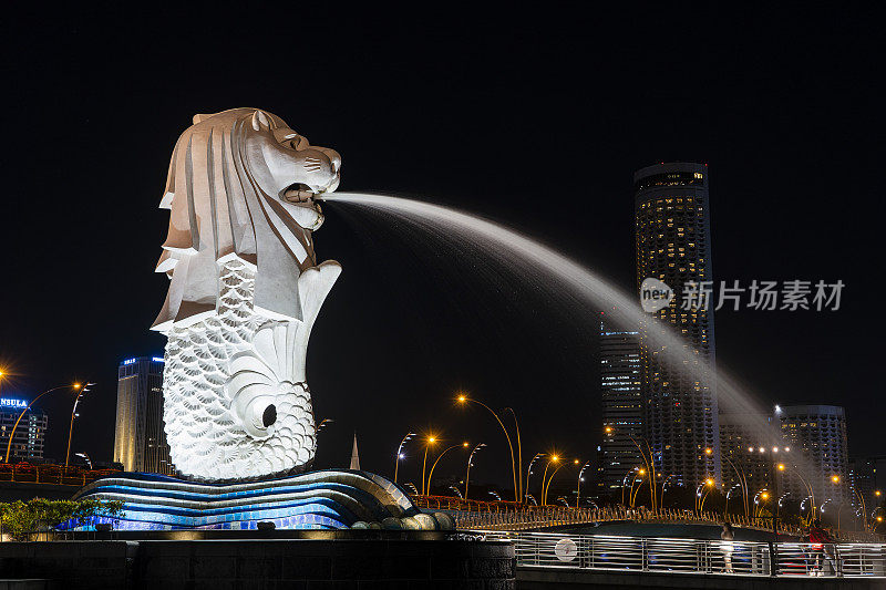 鱼尾狮雕像从它的嘴喷射水在新加坡市中心中心的鱼尾狮公园在晚上的时间在滨海湾