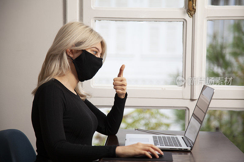年轻女子戴着面具在家用笔记本电脑进行视频通话