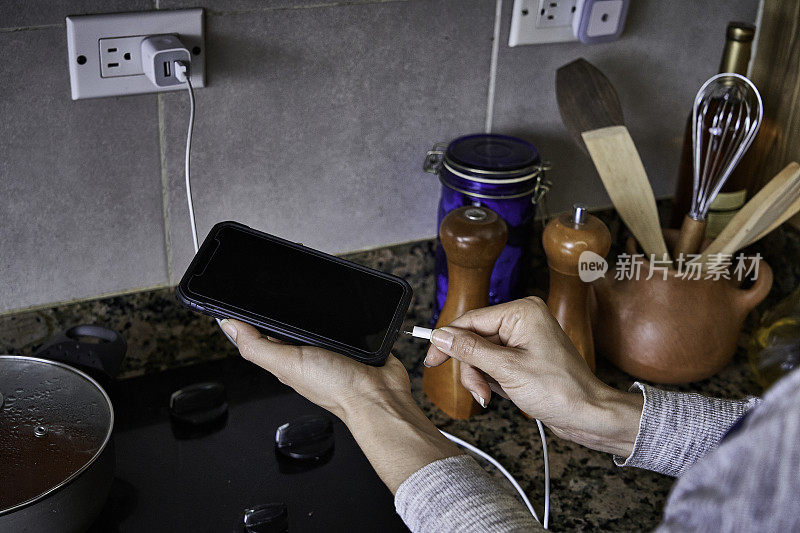 一名年轻女子在家中厨房里用手将充电电缆连接到智能手机上