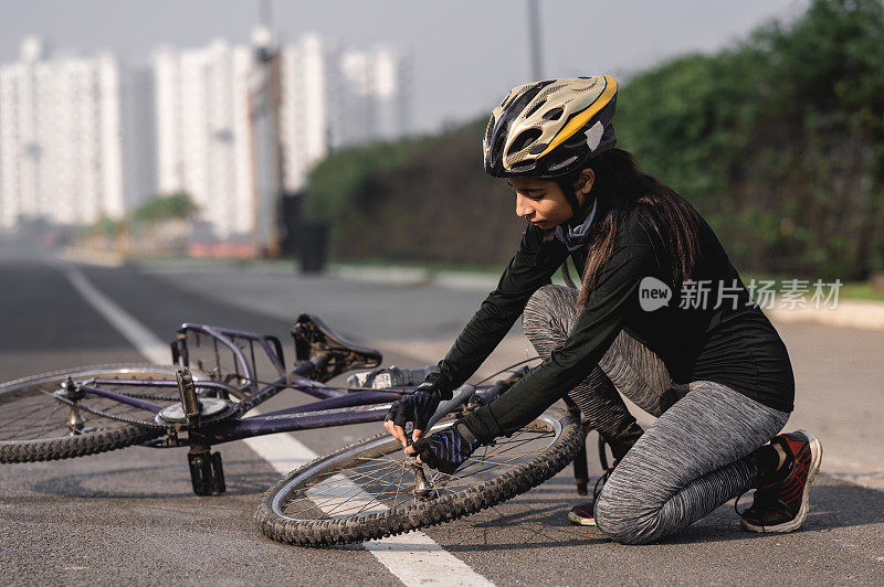 女运动员骑自行车时摔倒在路上，正在修理她的自行车。