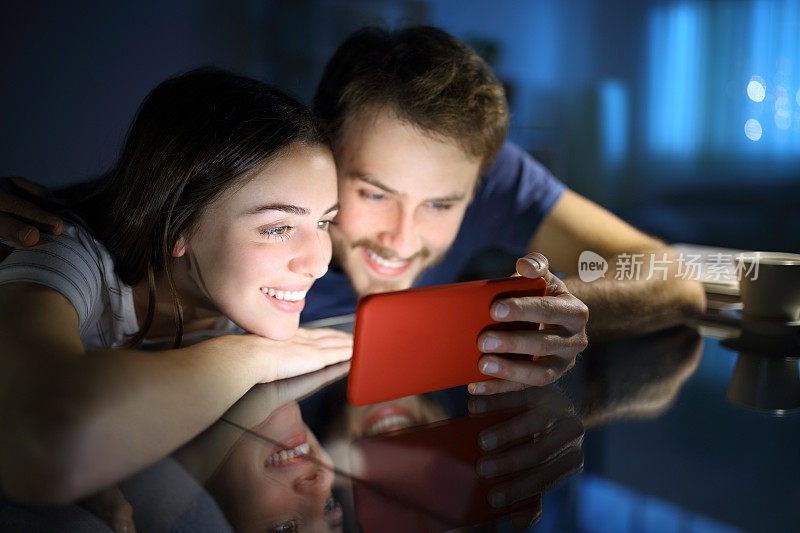 幸福的夫妇在晚上看手机上的媒体内容