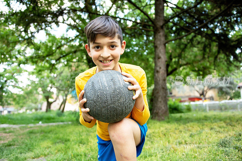 可爱的男孩在户外踢足球。那个孩子微笑着，手里拿着一个足球。体育概念的热情。