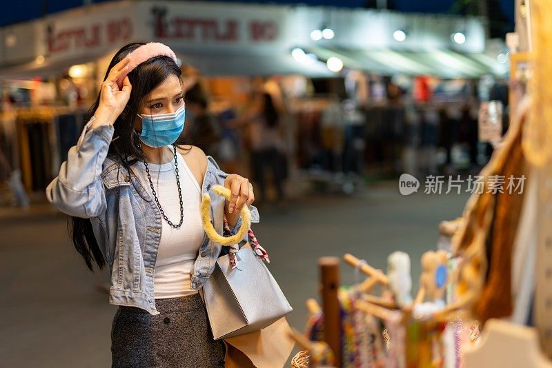 在泰国曼谷当地的夜市，一名戴着防护面膜的女性独自购物