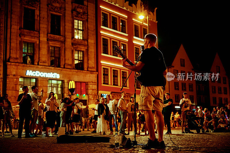 街头音乐表演。男人拿着吉他在夜晚的城市街道上唱着歌。波兰弗罗茨瓦夫——2021年8月14日