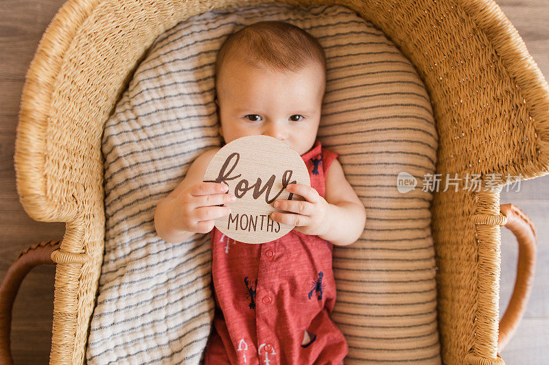 一个4个月大的小男孩穿着一件红色的航海服，躺在一个舒适的奶油色条纹棉毯上，在海草摩西篮子