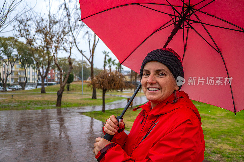 一个女人在雨天打着红伞走在公园里。肖像