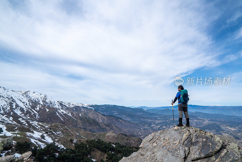 背景摄影师登山运动员是看风景，而持有登山杆在一个岩石山的顶峰。