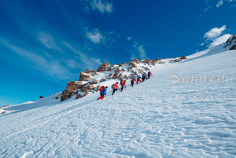 高山登山队在冬季在高海拔山峰上排成一行行走