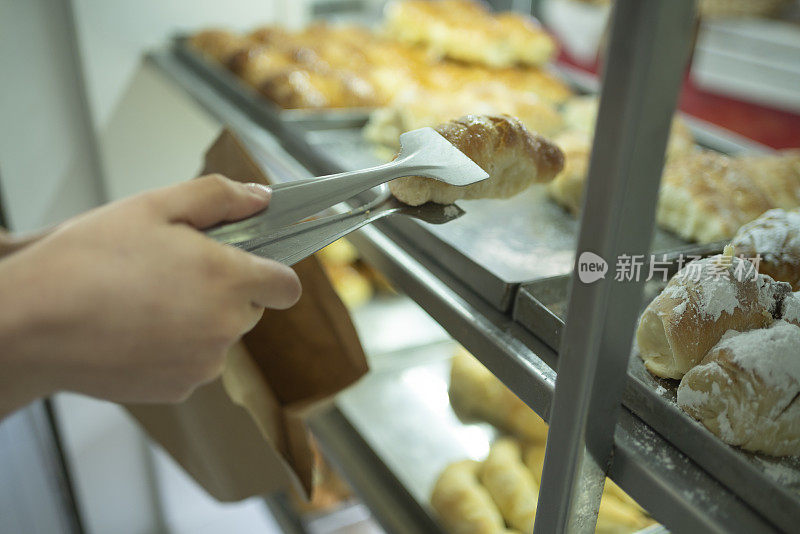 一位面包店女员工挑选甜面包并把它们放在纸袋上的细节