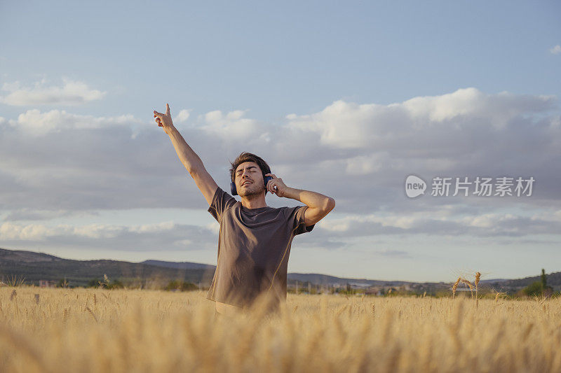 年轻英俊的男子在夏天的田野里听音乐