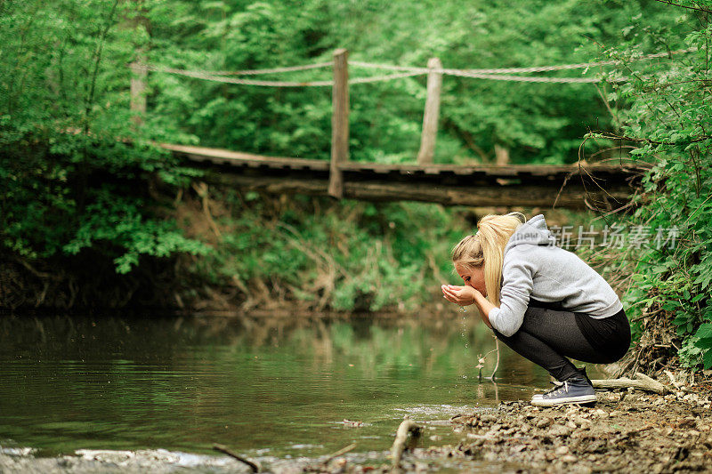 一个女人在喝着小溪里的淡水