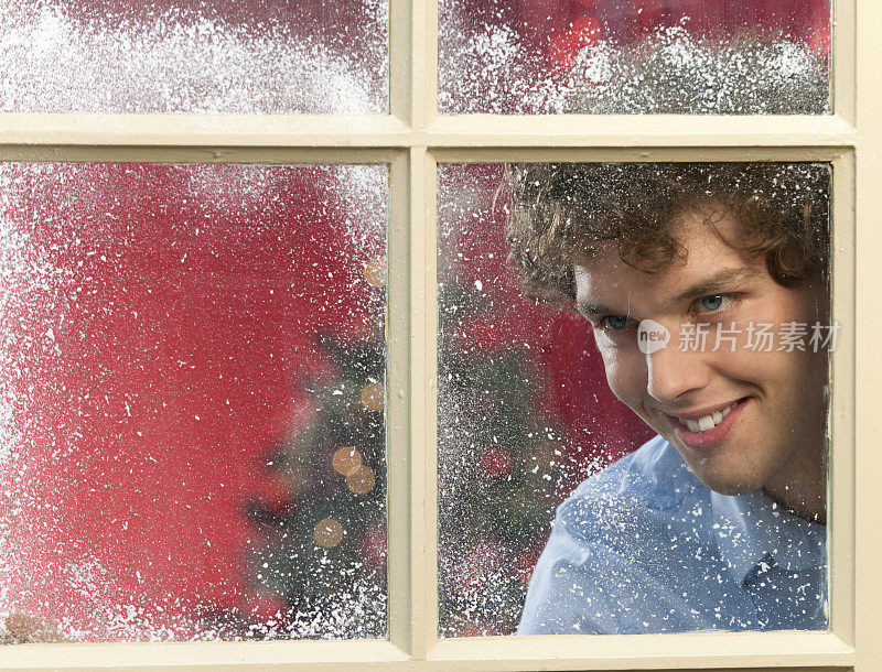快乐的年轻人在圣诞节透过下雪的窗户