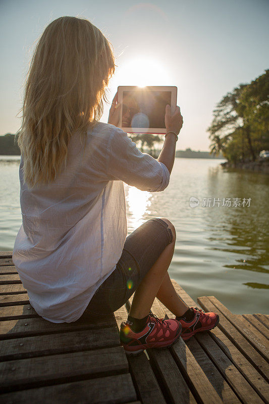 一名女子在湖边用平板电脑拍照