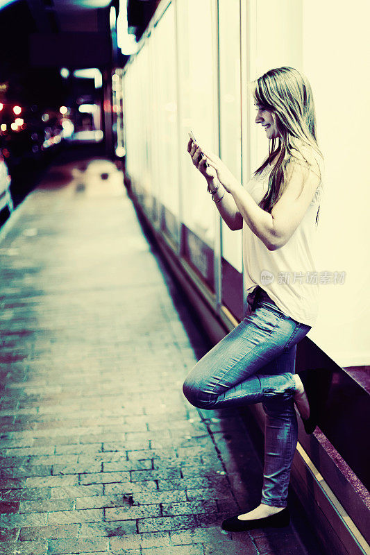 在空旷的夜间街道上，一个漂亮的女人低头看电话