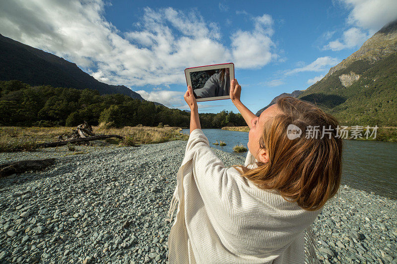 河边一位欢快的年轻女子正在使用电子平板电脑