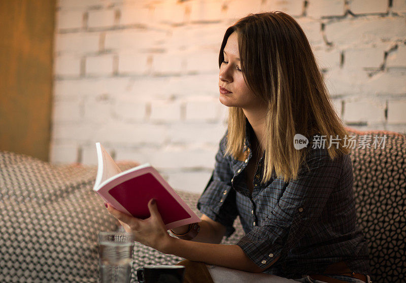 年轻女子放松与书在咖啡馆。