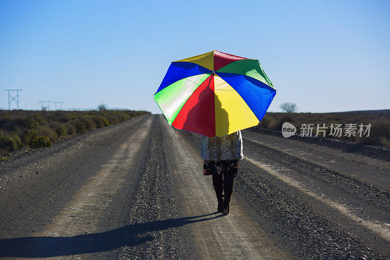 一个女人撑着伞，在阳光的照耀下走在碎石路上