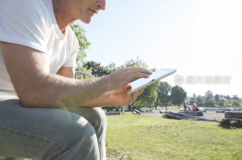 一名男子在公园长凳上休息，用着数码平板电脑