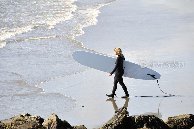 穿着潜水服的女人带着冲浪板出海