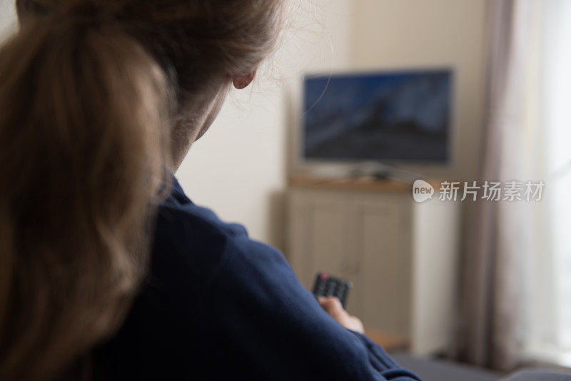 女人坐在沙发上，手里拿着遥控器，在家里的客厅里看电视