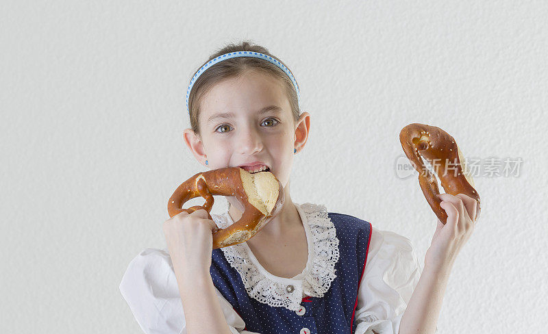 身着传统连衣裙的巴伐利亚小女孩咬着椒盐卷饼