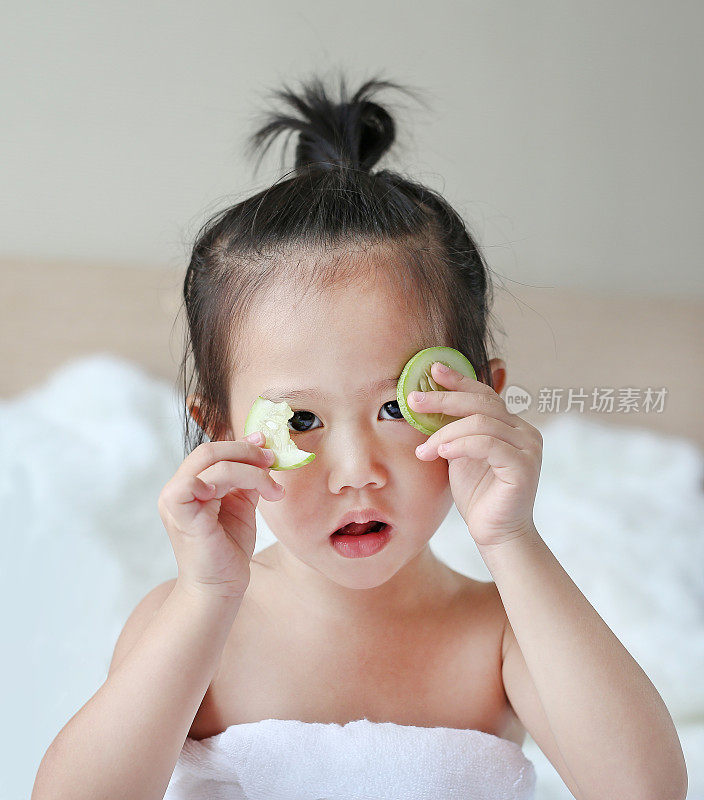 可爱的小女孩，眼睛里有一片黄瓜，皮肤护理的概念。