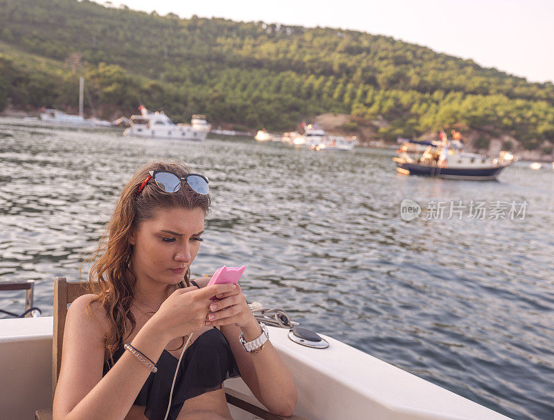 一名年轻女子在土耳其伊斯坦布尔哈贝里亚达附近的游艇上查看她的智能手机