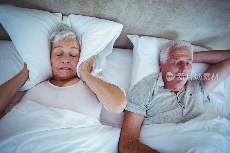 当丈夫在床上打鼾时，资深妇女用枕头堵住耳朵