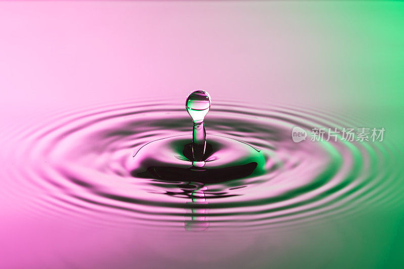 水滴近距离与同心涟漪在鲜艳的粉红色和绿色表面