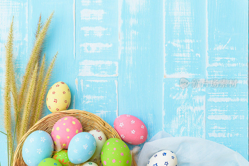 复活节快乐!色彩缤纷的复活节彩蛋在巢与纸星，花和羽毛在柔和的颜色明亮的蓝色和白色木制背景。
