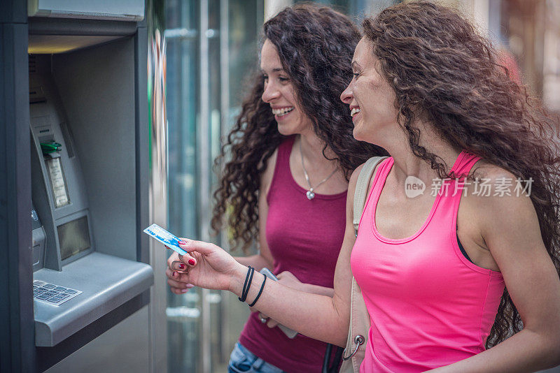 一对双胞胎姐妹在城市街道的自动取款机上取款