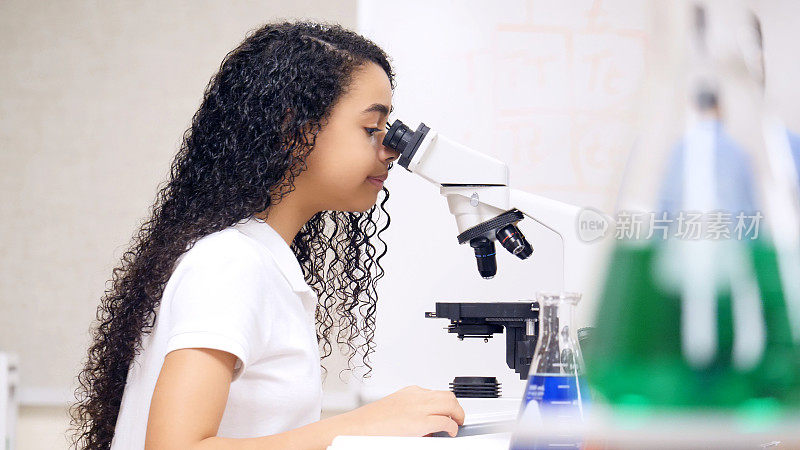 开朗的女学生在课堂上使用显微镜
