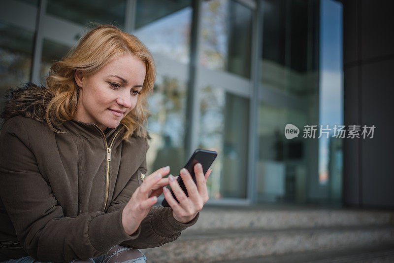 微笑的女人在户外看手机短信。