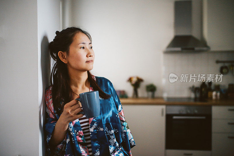 年轻的亚洲女性在家里放松，喝着早茶