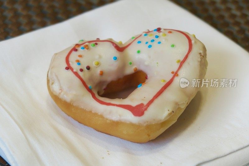 红白糖衣的爱心甜甜圈，餐巾上的彩虹点缀，情人节的甜甜圈蛋糕浪漫早餐照片