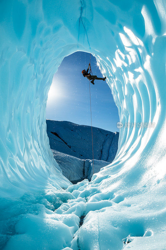 一名男子被吊在一根绳子上，在阿拉斯加边远地区的马塔努斯卡冰川的一个大冰洞里。