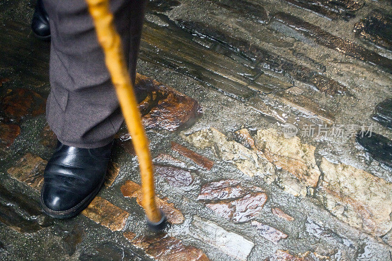 老人走路时，潮湿的石头地板在雨天，拄着拐杖走路。