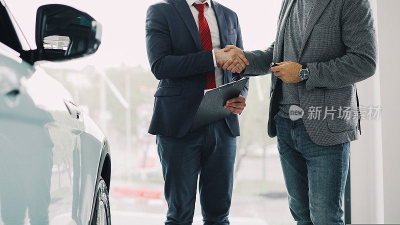 汽车展厅工作人员将车钥匙交给年轻的男性买家并握手，经销商正拿着证件并做手势。买卖运输概念。