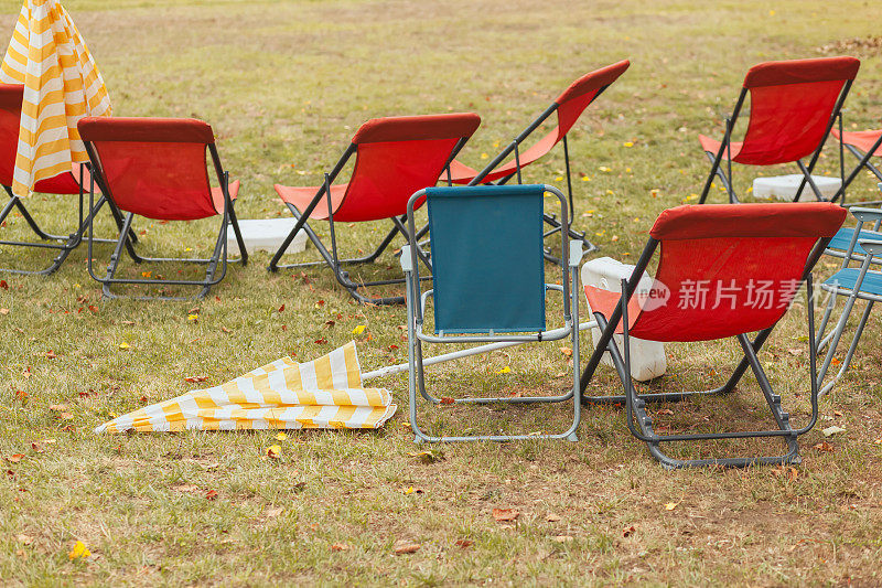 红色和蓝色的可折叠帆布椅，空的，闭合的条纹阳伞，夏末的概念