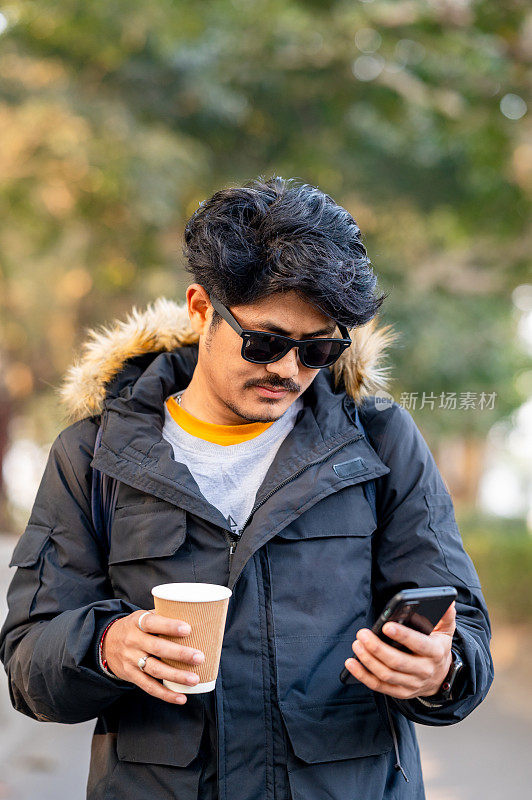 年轻人在冬天喝茶或咖啡，使用智能手机